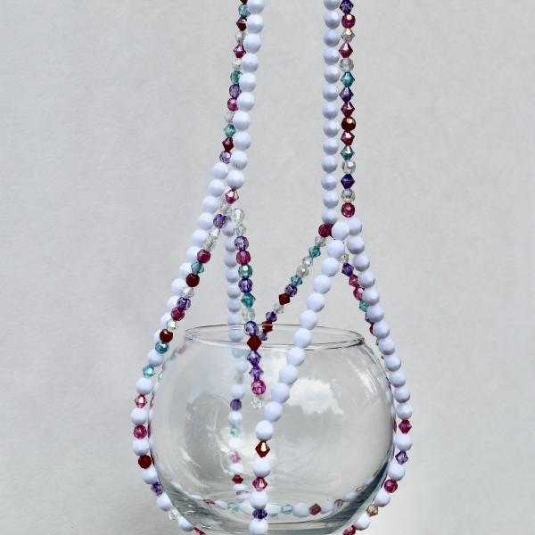 A playful, handmade plant hanger with jewel-toned beads adding a pop of color to a white plant pot.