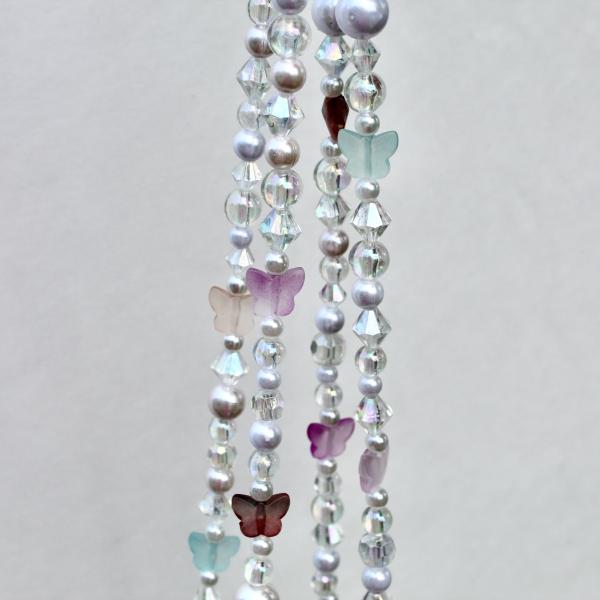 A macro shot showing the delicate details of the pastel butterfly, luminous pearl, and sparkling iridescent crystal beads.